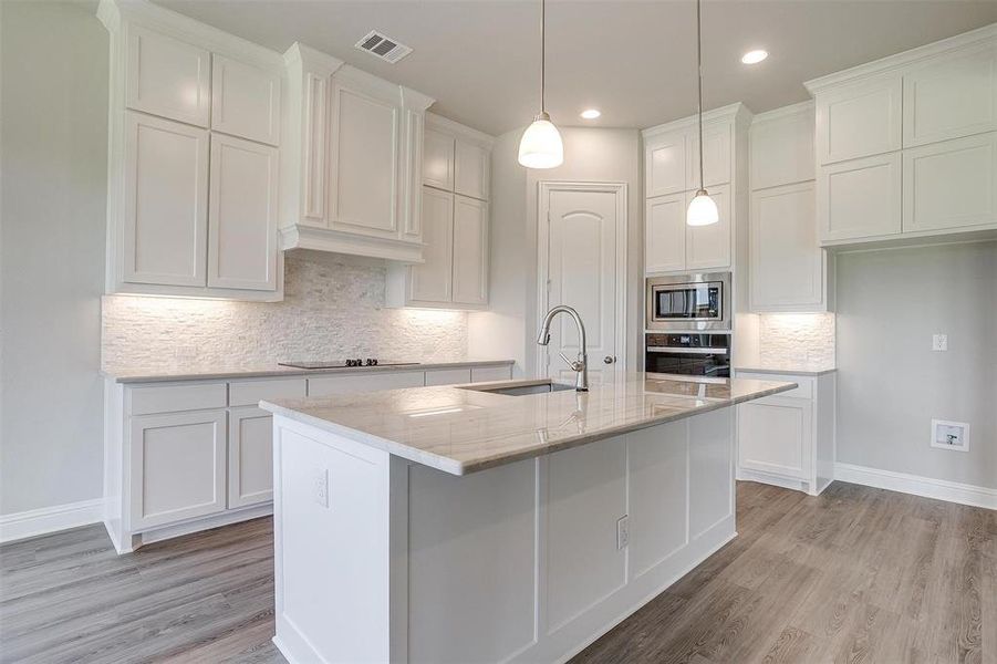 Kitchen with tasteful backsplash, stainless steel appliances, sink, light wood-type flooring, and an island with sink