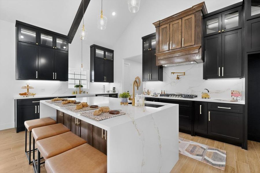 Kitchen with a center island with sink, glass fronted cabinets, a kitchen bar, dual tone cabinets, and hanging light fixtures