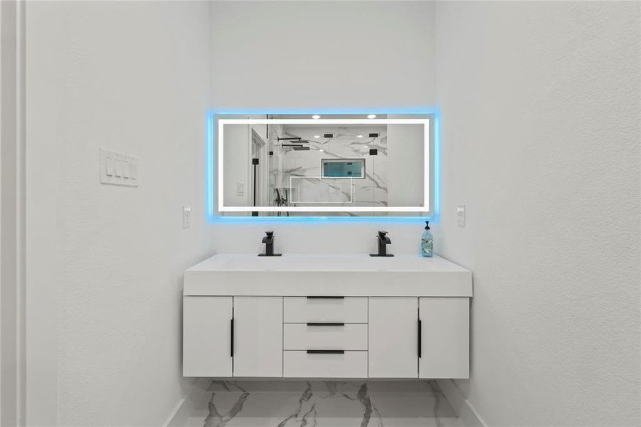 Full bathroom featuring double vanity, light marble finish flooring, and a marble finish shower Full bathroom featuring double vanity, light marble finish flooring, and a marble finish shower