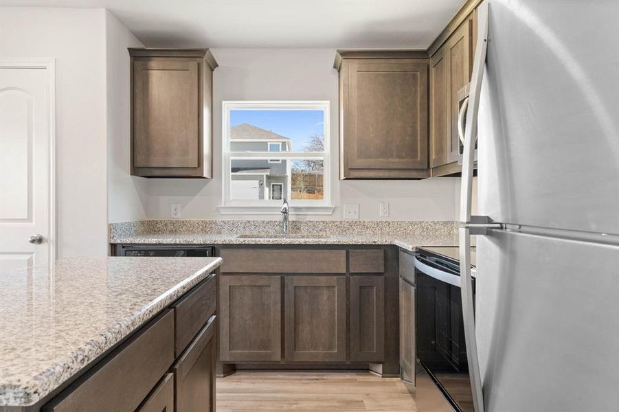 Kitchen with white refrigerator, sink, light stone countertops, light wood-type flooring, and electric range oven