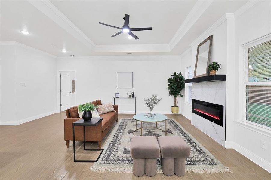 Living room with a high end fireplace, crown molding, light hardwood / wood-style flooring, ceiling fan, and a tray ceiling