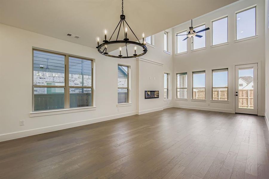 Unfurnished living room featuring dark wood-style flooring, a chandelier, ceiling fan, and a towering ceiling Unfurnished living room featuring dark wood-style flooring, a chandelier, ceiling fan, and a towering ceiling