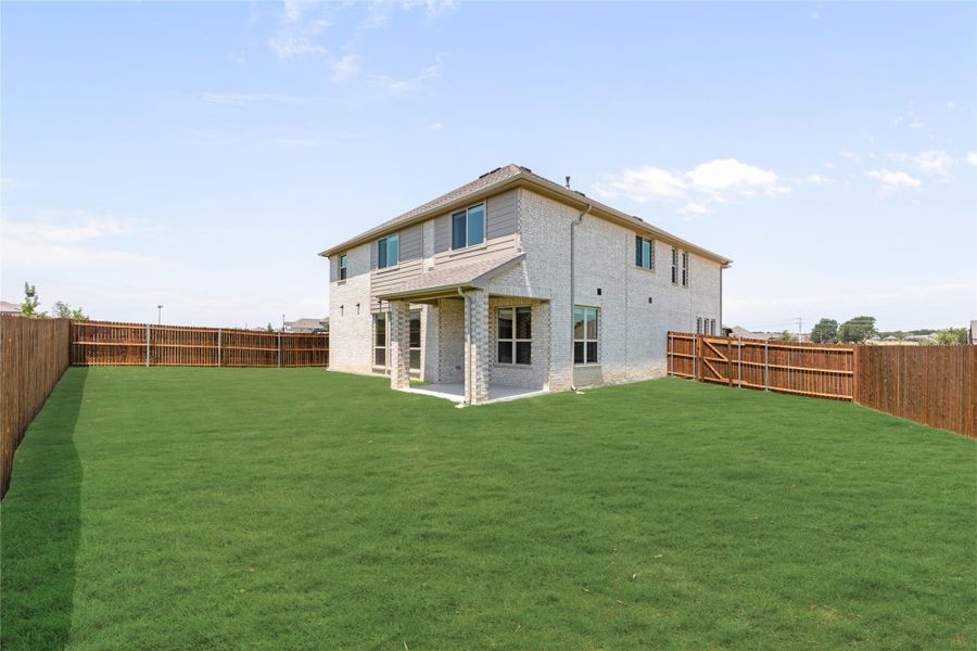 Two-story brick home with covered patio and large fenced backyard with green lawn