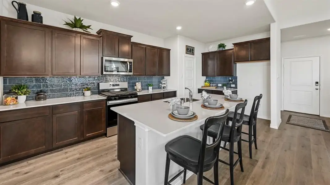 Kitchen featuring dark wood cabinetry, a subway tile backsplash, stainless steel appliances, a center island with sink, and wood-finish flooring