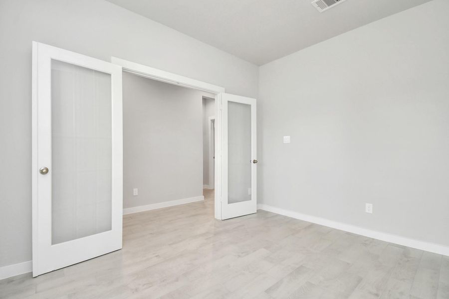 Experience the perfect blend of sophistication and warmth in this home office, boasting elegant wood-look tile flooring and flooded with natural light from expansive windows and French doors.