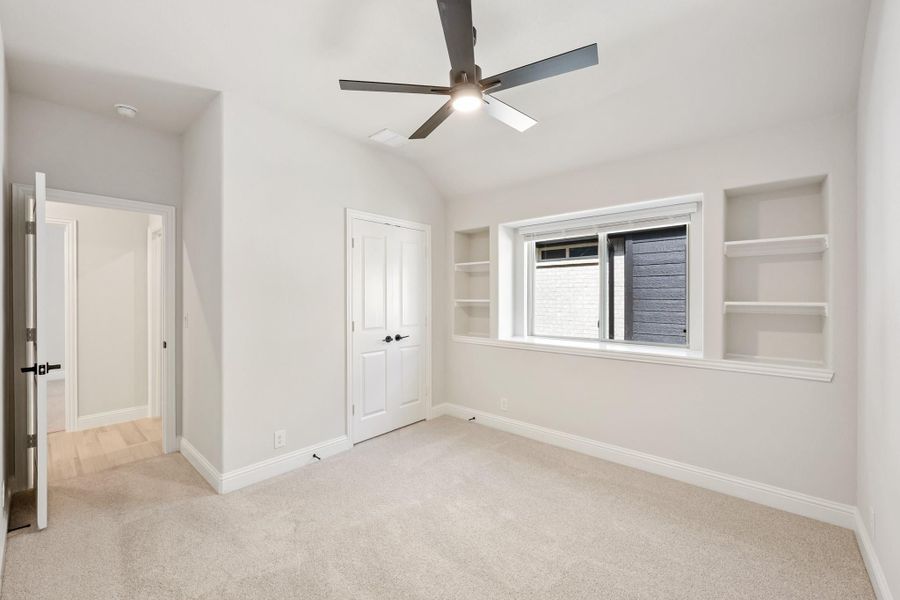 Empty bedroom with carpet, ceiling fan, built-in shelves, and a closet door Empty bedroom with carpet, ceiling fan, built-in shelves, and a closet door