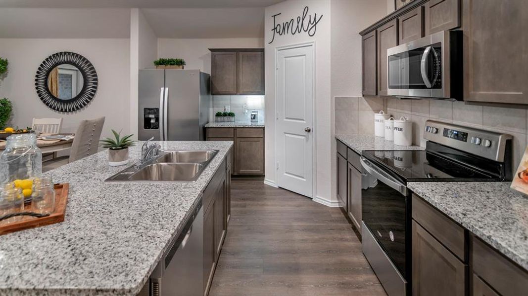 Kitchen with stainless steel appliances, dark wood-style floors, backsplash, and light stone countertops