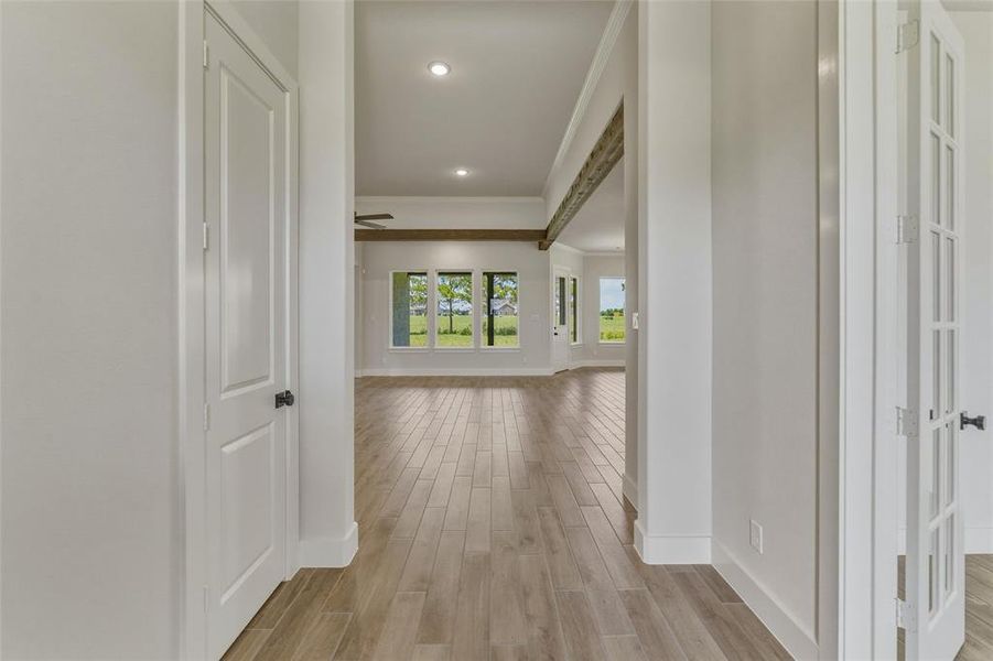 Bright interior hallway featuring wood-finish flooring, recessed lighting, and a white paneled door Bright interior hallway featuring wood-finish flooring, recessed lighting, and a white paneled door
