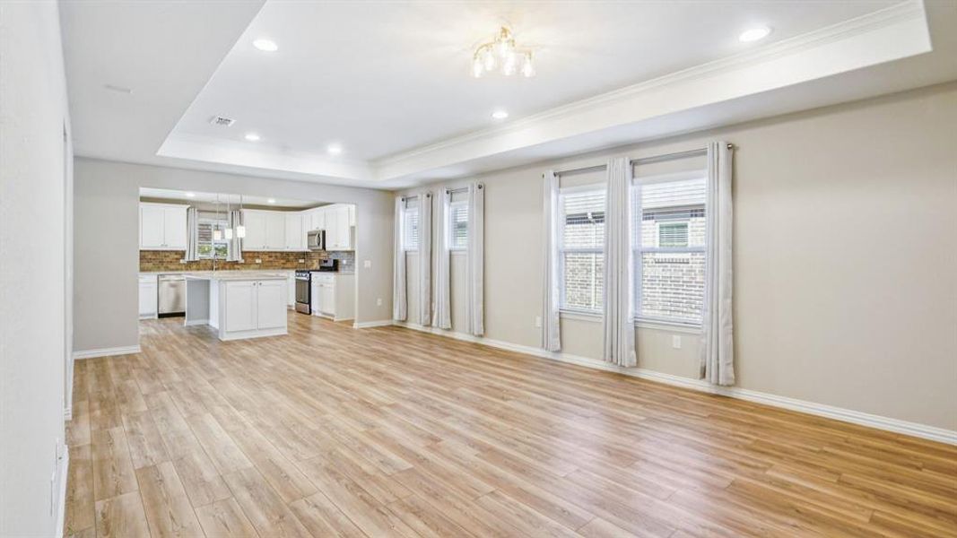 Unfurnished living room featuring a raised ceiling, plenty of natural light, recessed lighting, light wood finished floors, and crown molding Unfurnished living room featuring a raised ceiling, plenty of natural light, recessed lighting, light wood finished floors, and crown molding