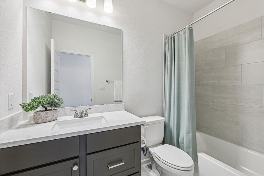 Well-appointed bathroom featuring a vanity with a white countertop and a rectangular undermount sink, a large mirror, and a bathtub with light gray tiled walls