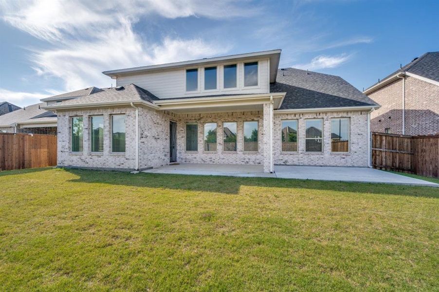 Spacious backyard featuring a large concrete patio, a covered patio area, and a brick exterior with multiple windows