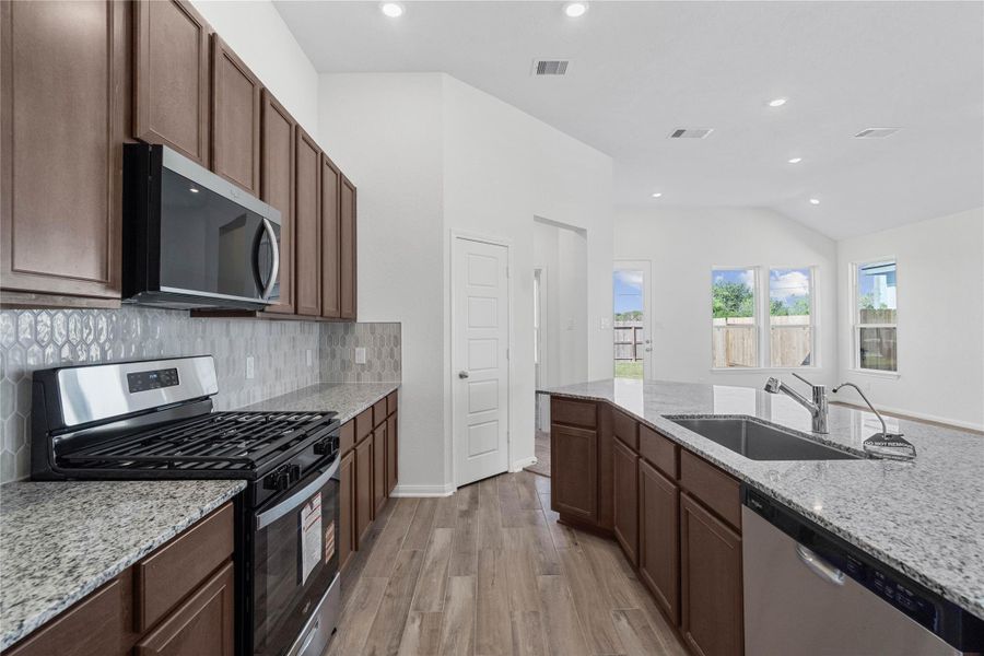 A true chef’s dream, this expansive kitchen boasts high ceilings, rich stained wood cabinets, granite countertops, stainless steel appliances, a modern tile backsplash, recessed lighting, extended counter space, an island with a large single sink, and a pantry—all with a clear view of the spacious Great Room.