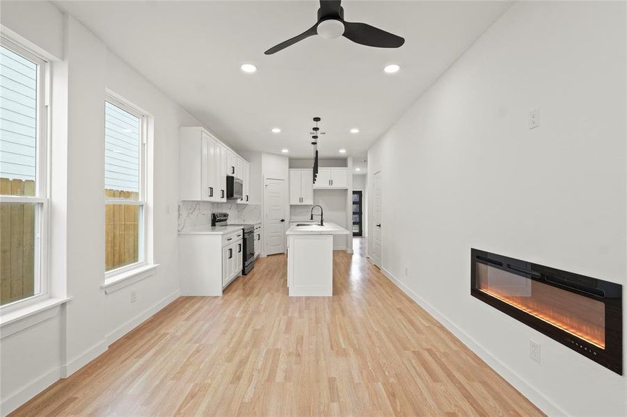 Kitchen with white cabinetry, decorative light fixtures, a center island with sink, stainless steel appliances, and light hardwood / wood-style floors