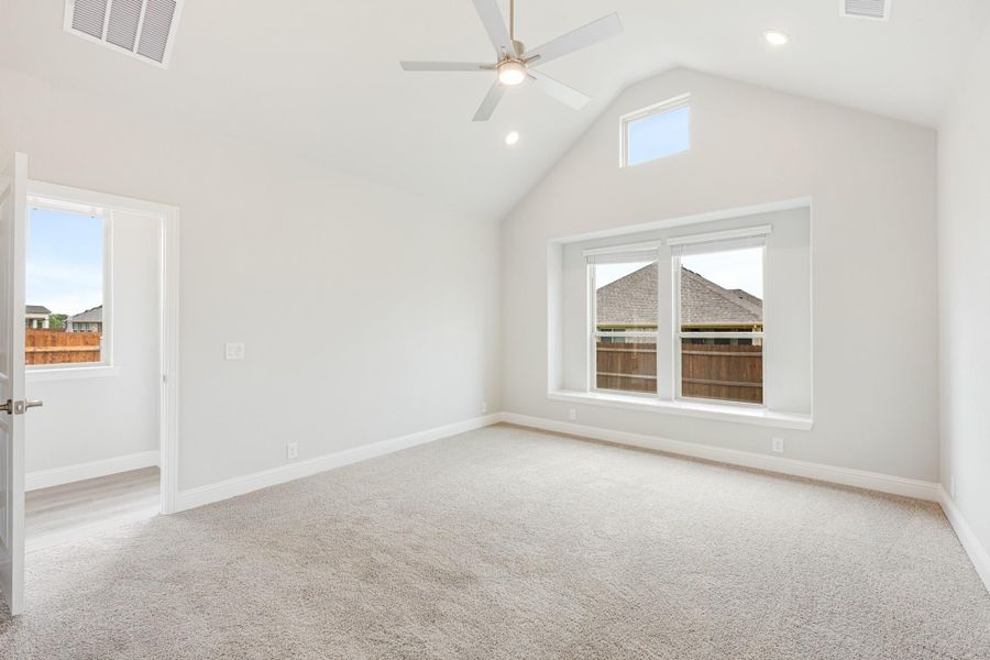Empty bedroom with vaulted ceiling, ceiling fan, carpet flooring, and large windows