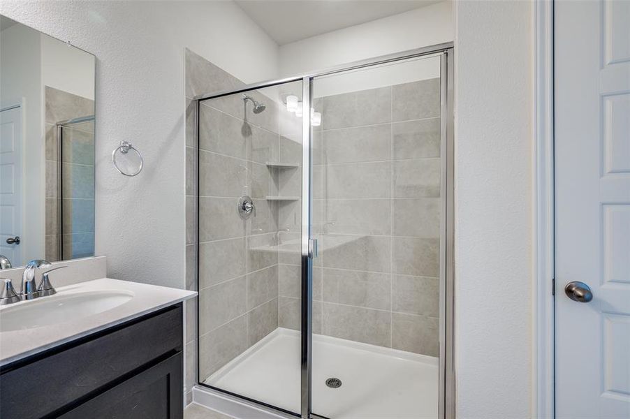 Full bathroom featuring a stall shower, a textured wall, and vanity