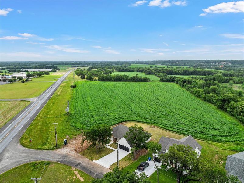 Expansive green acreage with a paved road frontage, bordering cultivated fields and mature tree lines
