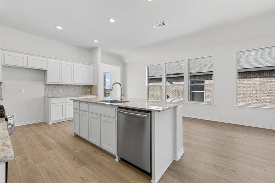 Kitchen featuring white cabinets, appliances with stainless steel finishes, light stone counters, light wood-type flooring, and vaulted ceiling