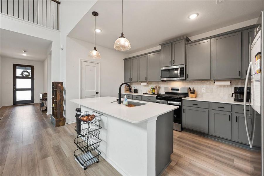 Modern kitchen featuring gray cabinetry, stainless steel appliances, a center island with a white countertop, and wood-finish flooring