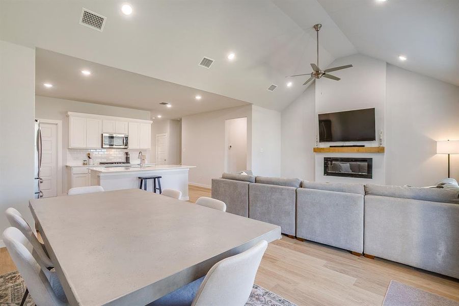 Dining space with light wood-style floors, a glass covered fireplace, recessed lighting, ceiling fan, and high vaulted ceiling Dining space with light wood-style floors, a glass covered fireplace, recessed lighting, ceiling fan, and high vaulted ceiling