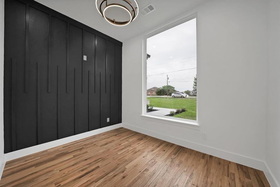 This room features hardwood flooring, a statement accent wall with vertical paneling, and a large window providing views of the outdoors