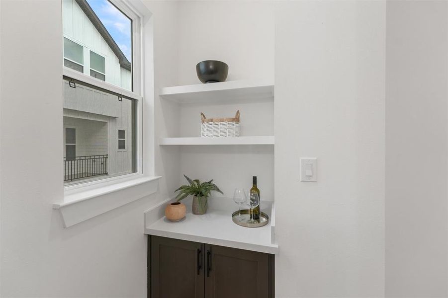 Your modern dry bar area with built-in shelving and a quartz countertop. There's a large window providing natural light, and the space features clean lines and a simple, elegant design. This dry bar is in Plan B only.