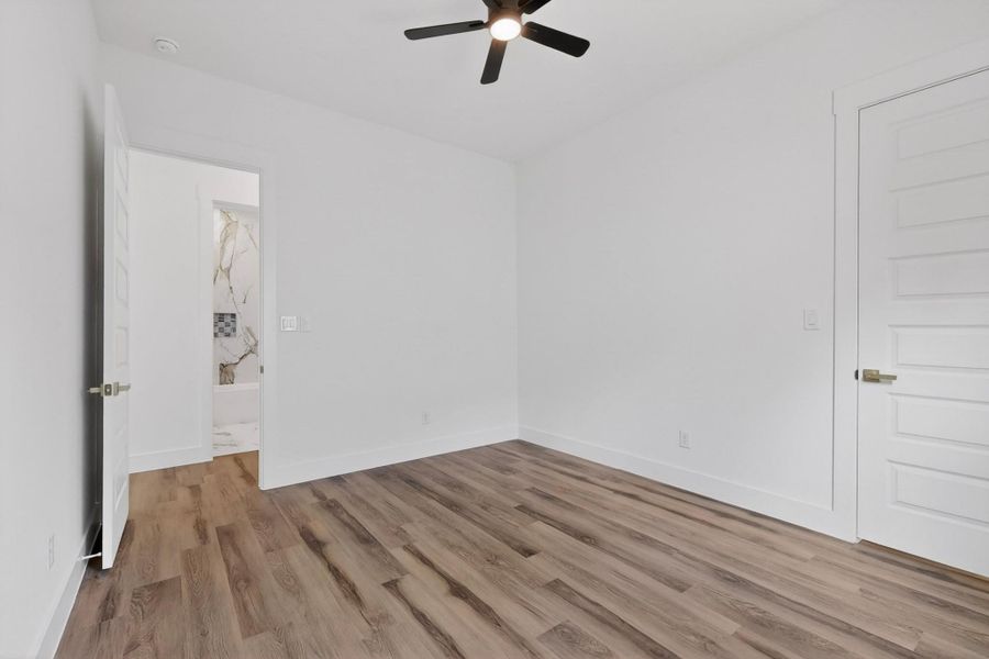 A well-lit bedroom with durable wood flooring and a modern ceiling fan for comfort.