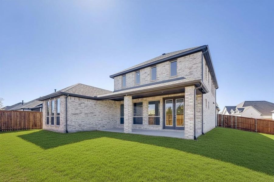 Rear exterior of a two-story home featuring light-toned brick masonry and a covered patio