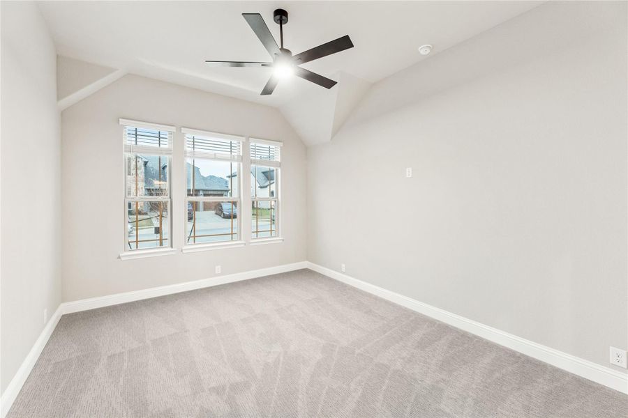 Empty bedroom with vaulted ceiling, ceiling fan, carpet flooring, and triple windows