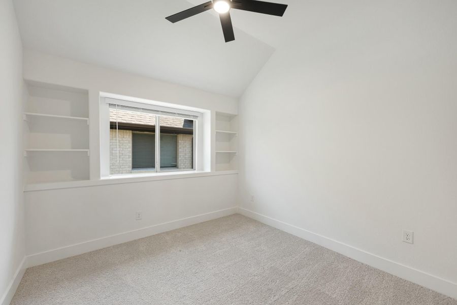 Empty bedroom with vaulted ceiling, ceiling fan, built-in shelves, and carpet flooring