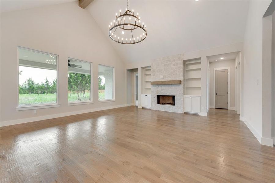 Unfurnished living room featuring beamed ceiling, built in shelves, a stone fireplace, and light hardwood / wood-style flooring