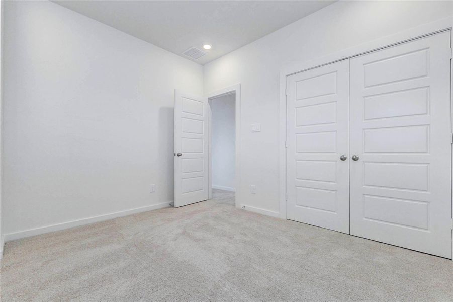Secondary bedroom with neutral carpet, white walls, recessed lighting, and double closet doors for convenient storage. The clean, move-in-ready design provides a versatile space that can easily serve as a guest room, child’s bedroom, home office, or quiet retreat.