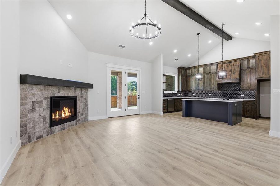 Open-concept interior featuring light wood-finish flooring, vaulted ceilings, and a corner fireplace with stone tile surround