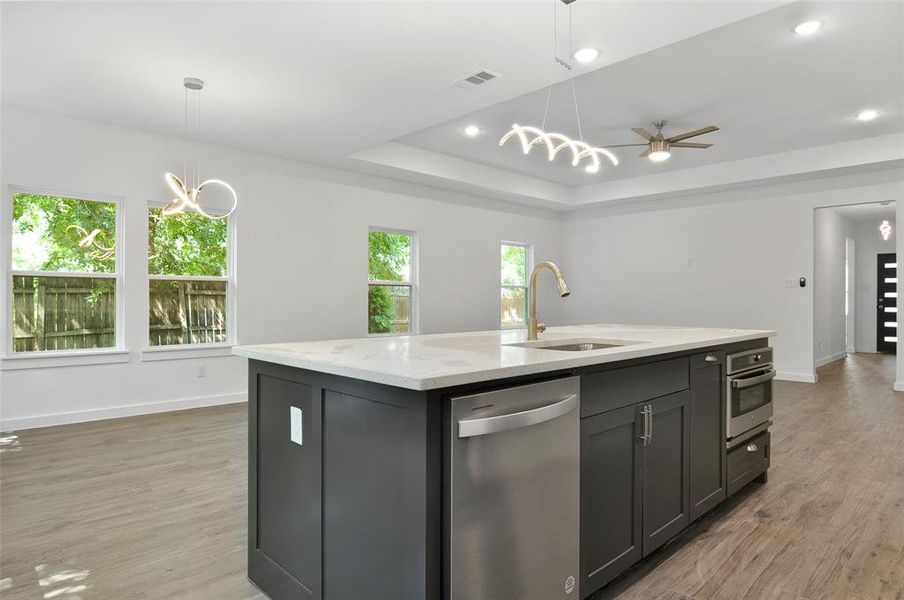 Kitchen featuring light hardwood / wood-style flooring, ceiling fan with notable chandelier, an island with sink, stainless steel appliances, and a raised ceiling