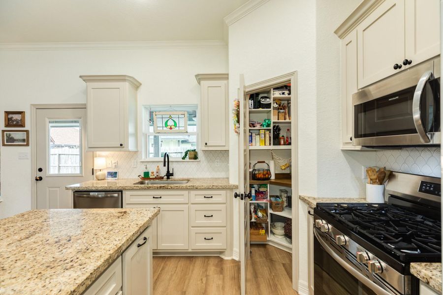 This kitchen features modern appliances, granite countertops, and ample storage with a walk-in pantry. The space is bright and welcoming, with a charming stained glass window above the sink.