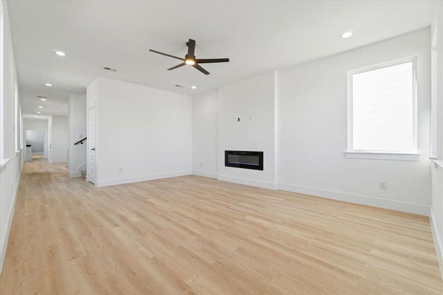 Unfurnished living room featuring light wood-type flooring, a glass covered fireplace, visible vents, and recessed lighting