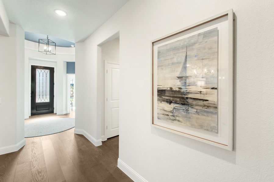 Bright entryway hallway with hardwood floors, framed wall art, and glass-panel front door with pendant light overhead