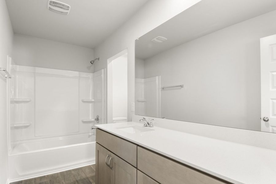 Image of a bathroom with brown cabinets and a white vanity with a white vanity and large mirror with white vinyl shower and tub Image of a bathroom with brown cabinets and a white vanity with a white vanity and large mirror with white vinyl shower and tub