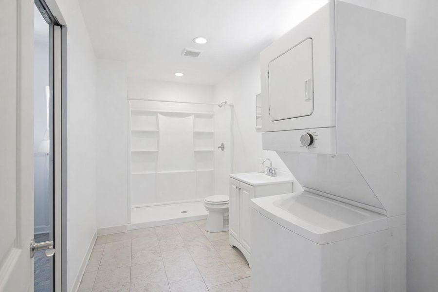 Bathroom featuring a shower stall, toilet, vanity with sink, and a stacked washer and dryer unit