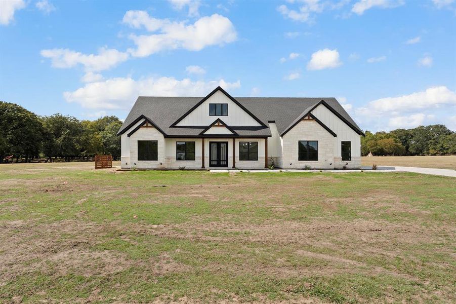 Modern farmhouse featuring a front lawn, roof with shingles, board and batten siding, and stone siding