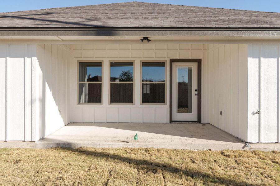 Property entrance featuring roof with shingles, a patio, and a yard