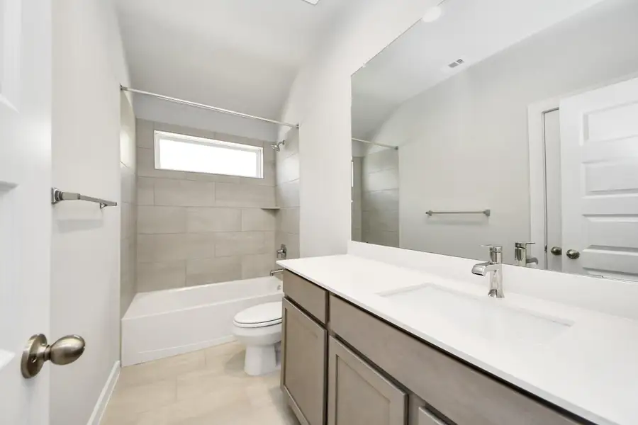 Secondary bath features tile flooring, bath/shower combo with tile surround, light stained wood cabinets, beautiful light countertop. Sample photo of completed home with similar floor plan. Actual colors and selections may vary.