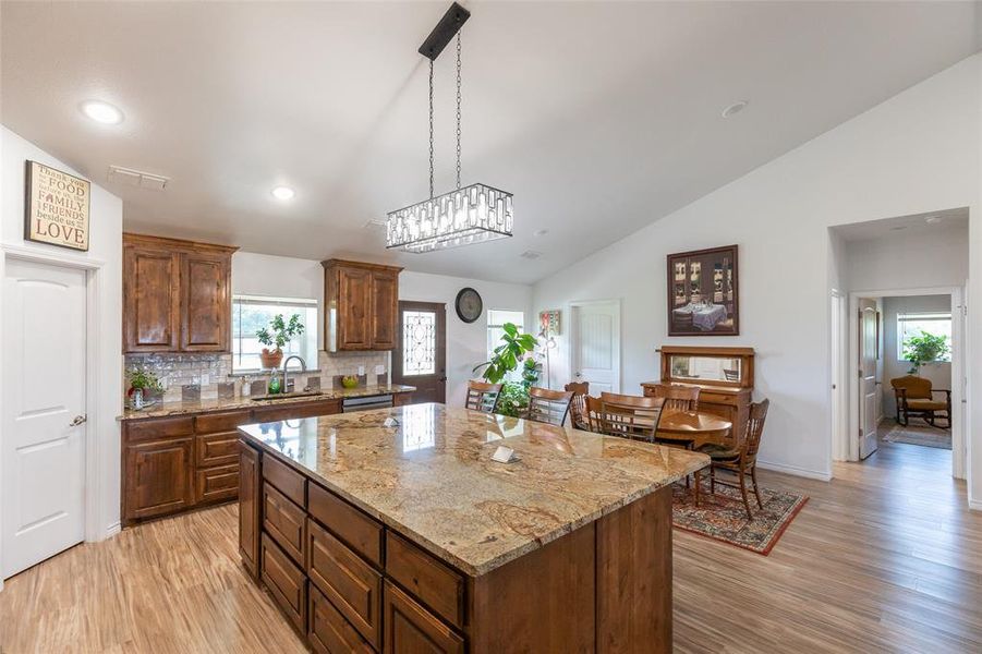 Kitchen featuring a large island with a stone countertop, wood-finish flooring, wood cabinetry, and a tile backsplash Kitchen featuring a large island with a stone countertop, wood-finish flooring, wood cabinetry, and a tile backsplash