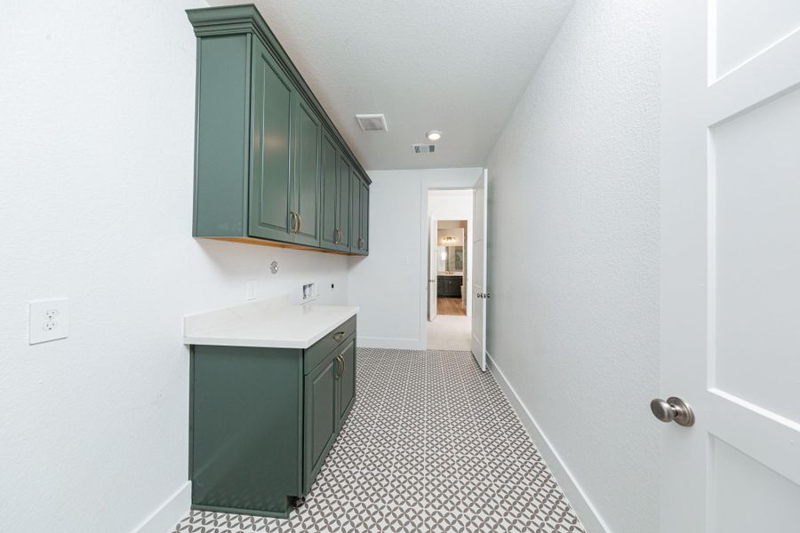 This bright and functional laundry room is conveniently located right off the primary walk-in closet and is ready for your appliances. It features clean white walls, trim, cabinets, and tile flooring.