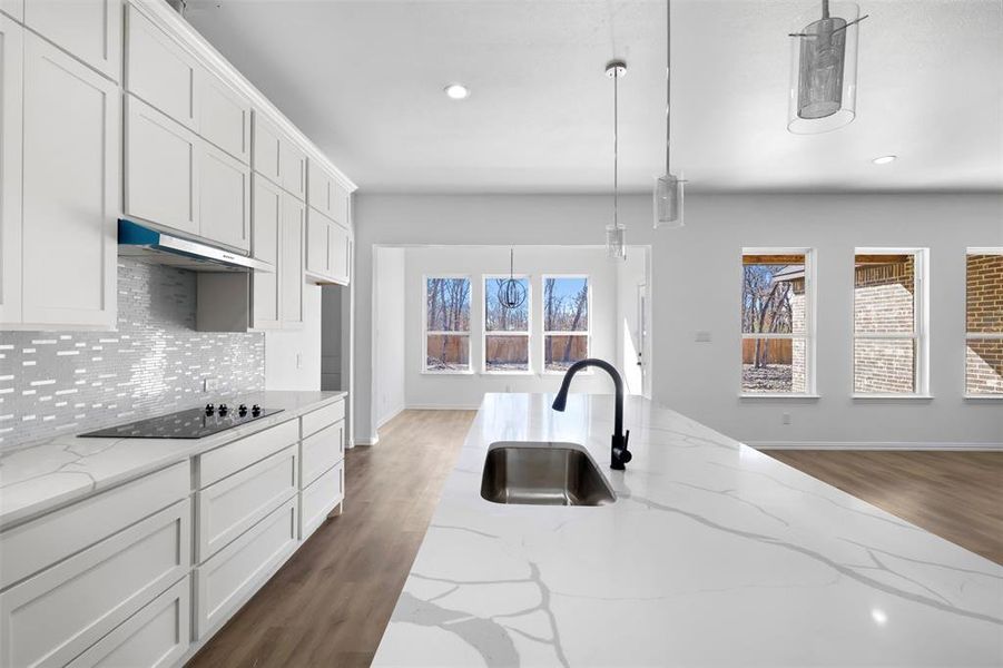 Kitchen featuring pendant lighting, white cabinets, sink, black electric cooktop, and light stone counters