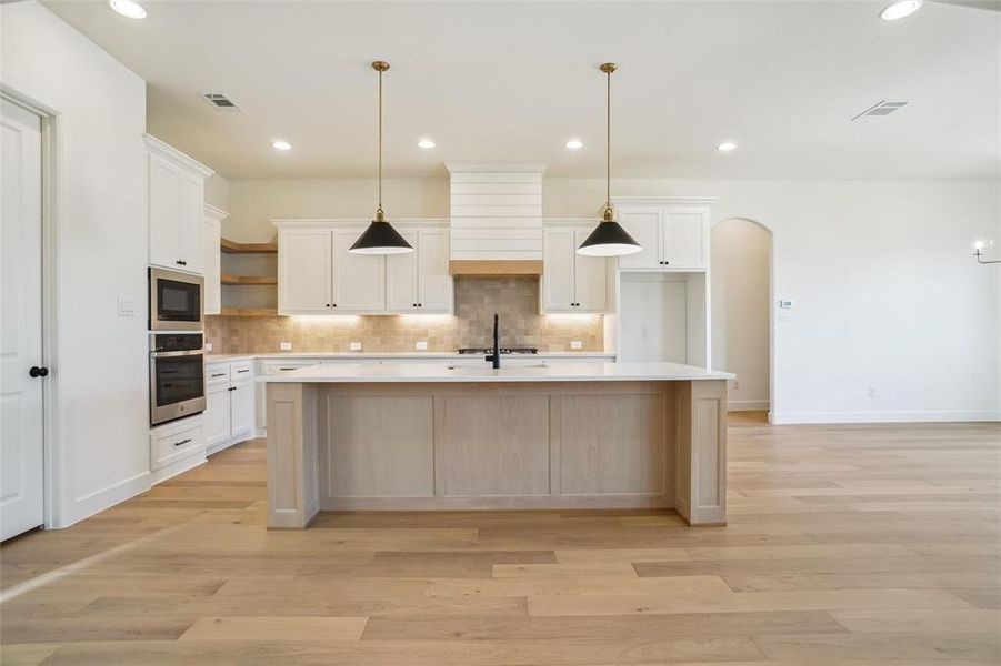 Kitchen featuring white cabinets, light hardwood / wood-style flooring, an island with sink, and appliances with stainless steel finishes