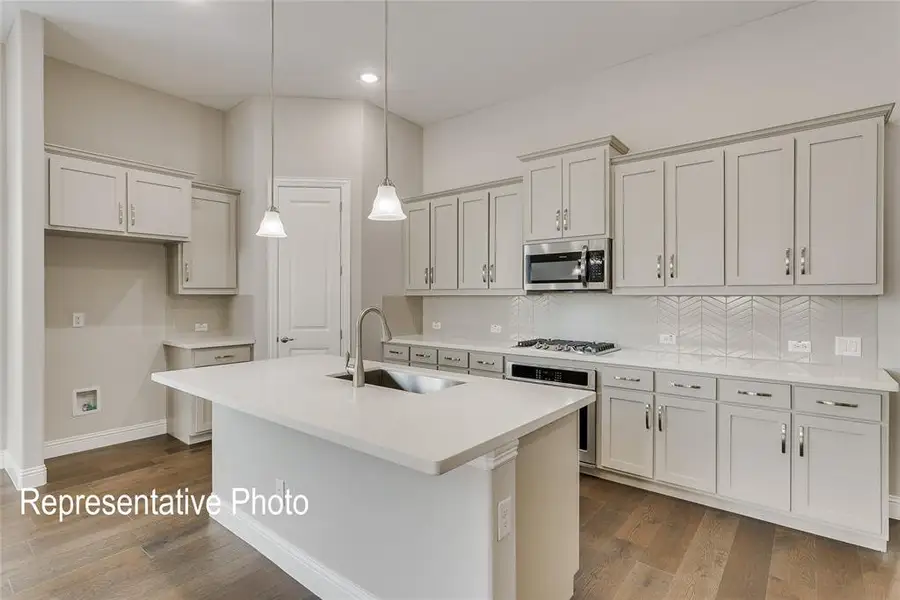 Kitchen featuring light-toned cabinetry, quartz countertops, a herringbone tile backsplash, stainless steel appliances, and wood-finish flooring