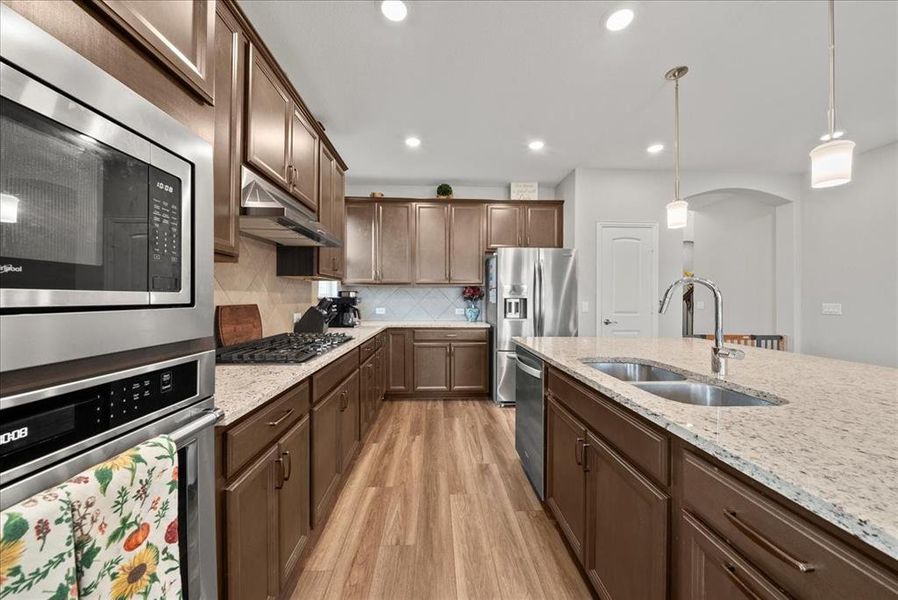 Kitchen featuring sink, stainless steel appliances, light stone counters, light luxury vinyl flooring, pendant and recess lighting.