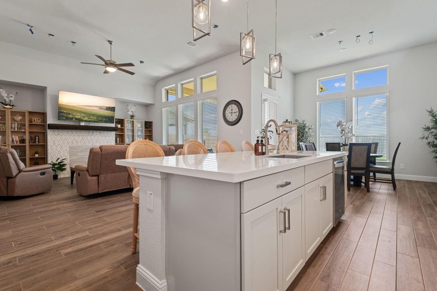 This photo showcases a modern open-concept living space with a bright, airy feel looking over the kitchen island. It features a spacious kitchen island with white cabinetry, pendant lighting, and a sleek countertop. The living area includes comfortable seating, a wall-mounted TV above a fireplace, and large windows that bring in natural light. The dining area is adjacent, offering a seamless flow for entertaining and group activities. This photo showcases a modern open-concept living space with a bright, airy feel looking over the kitchen island. It features a spacious kitchen island with white cabinetry, pendant lighting, and a sleek countertop. The living area includes comfortable seating, a wall-mounted TV above a fireplace, and large windows that bring in natural light. The dining area is adjacent, offering a seamless flow for entertaining and group activities.