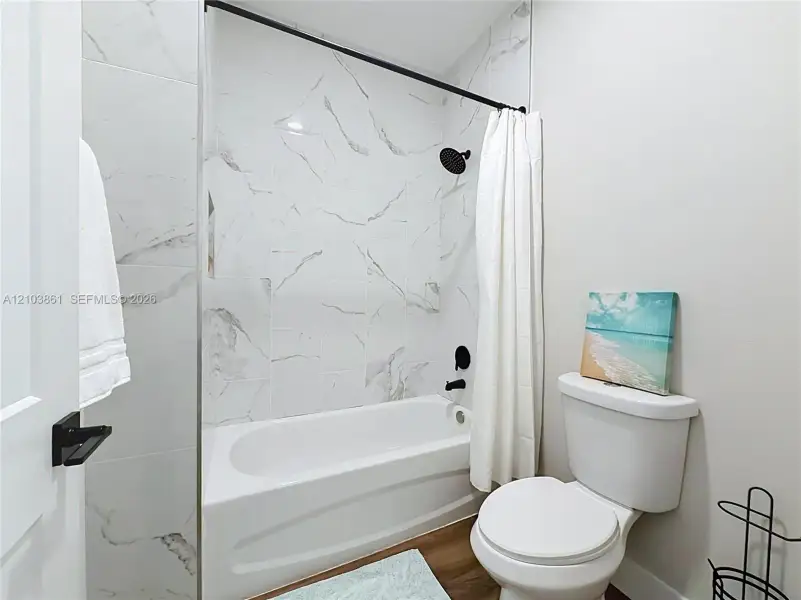 Bathroom featuring a tub-shower combination with floor-to-ceiling large-format veined tile surround, matte black rainfall showerhead, matching matte black plumbing fixtures, and wood-finish flooring