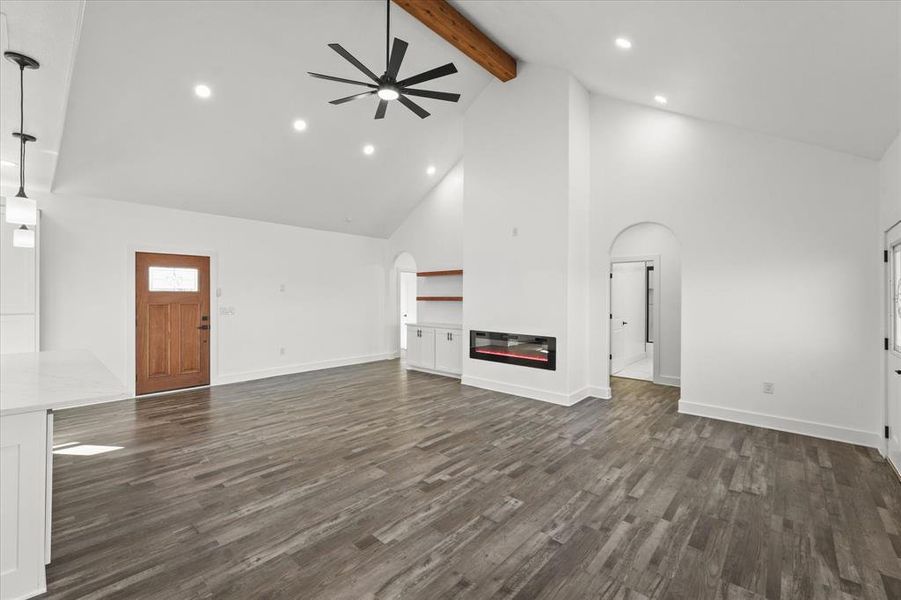 Unfurnished living room featuring ceiling fan, beam ceiling, dark hardwood / wood-style flooring, and high vaulted ceiling